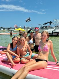 A joyful group of children and adults enjoy a sunny day paddleboarding and swimming in shallow waters, creating lasting memories together.