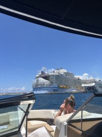 A woman relaxes on a boat while admiring the grandeur of cruise ships docked nearby, capturing the essence of a perfect day on the water.