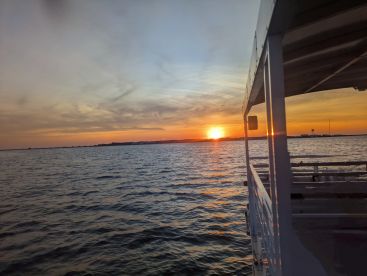 A serene sunset view from the deck of a boat, showcasing the tranquil waters and a picturesque horizon — perfect for evening cruises.