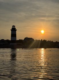 A stunning sunset casts a warm glow over a lighthouse, creating beautiful reflections on the water — a picturesque scene perfect for evening boat trips.