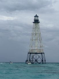 A lighthouse stands prominently in the water, surrounded by boats and a cloudy sky, creating a scenic maritime view.