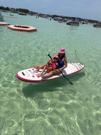 A mother and daughter enjoy paddleboarding in crystal-clear waters, capturing a perfect family moment on a sunny day.