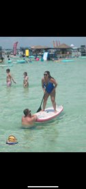 A lively scene of people enjoying paddleboarding and swimming in clear waters, perfect for a fun day at the beach.