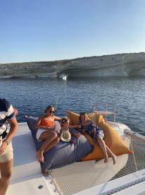 A joyful family enjoys a relaxing moment on a catamaran, lounging on oversized cushions with stunning coastal views in the background — perfect for memorable summer outings.