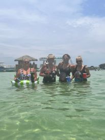 A fun group of friends enjoys a lively day in the water, holding drinks and celebrating at a sandbar — perfect for summer outings and memorable gatherings.