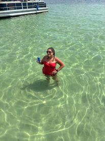 A woman enjoys a refreshing drink while wading in crystal-clear waters next to a pontoon boat, capturing the essence of a fun day on the water.