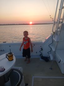 A child stands on the deck of a boat during a beautiful sunset, capturing a memorable family moment on the water.