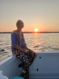 A woman enjoys a serene sunset on a boat, capturing the moment with her phone — a perfect scene for relaxation and reflection on the water.