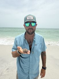 A man holds a unique shell on the beach, showcasing a close encounter with marine wildlife — perfect for beachcombing enthusiasts.