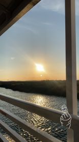 A serene sunset view over a tranquil waterway, framed by the railing of a boat — perfect for capturing the beauty of nature while cruising.