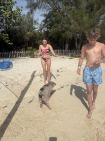 Two young people interact with a friendly pig on the beach, capturing a fun wildlife experience in a tropical setting.