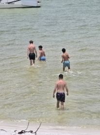 A group of young men wade into the shallow waters near a pontoon boat, enjoying a fun day at the beach — perfect for summer adventures and water activities.