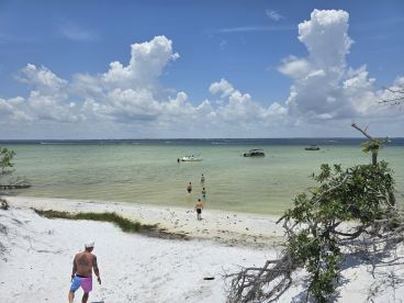 A lively beach scene with people enjoying the water and boats anchored nearby, perfect for a fun sandbar stop and group activities.