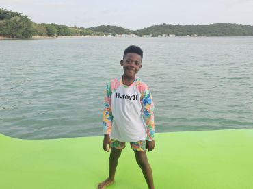 A cheerful child poses on a vibrant green surface by the water, capturing the joy of a fun day at the beach.