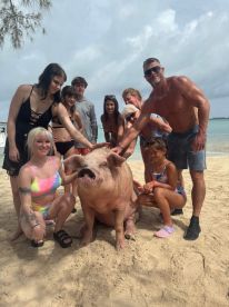 A lively group interacts with a friendly pig on the beach, creating a memorable wildlife experience — perfect for animal lovers and adventure seekers.