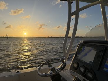 A serene view from the helm of a boat at sunset, showcasing the navigational equipment and the shimmering water, perfect for evening cruises.