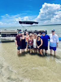 A cheerful group enjoys a sandbar stop, posing together in shallow water with their pontoon boat in the background — a perfect day of fun and relaxation on the water.