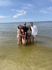 A joyful group of friends and family enjoys a sunny day at the beach, wading in the water and creating lasting memories together.