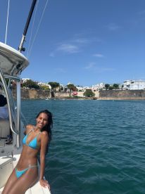 A young woman poses on the deck of a boat against a picturesque coastal backdrop, capturing the essence of a fun day on the water.
