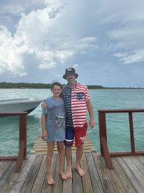 A father and daughter pose together on a dock with a boat in the background, capturing a memorable family moment by the water.
