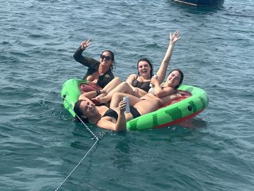 A fun group of friends enjoys a sunny day on a floating mat in the water, celebrating with drinks and laughter — perfect for summer adventures.