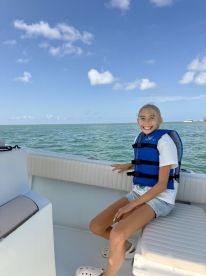 A young girl smiles while seated on a boat, wearing a life jacket, enjoying a sunny day on the water — perfect for family outings and water adventures.
