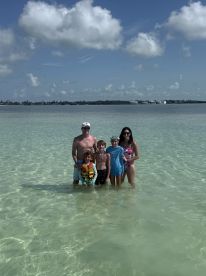 A joyful family poses together in shallow waters, enjoying a fun day at the beach — perfect for creating lasting memories during summer vacations.