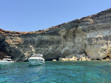Two boats anchored near a stunning rocky coastline, showcasing the beautiful turquoise waters — a perfect spot for a day of exploration and relaxation.