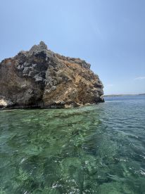 A rocky outcrop rises above clear waters, creating a picturesque coastal scene. The image lacks clarity, making it difficult to discern details.