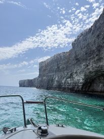 A stunning view of a rugged coastline from the bow of a boat, showcasing the clear turquoise waters and dramatic cliffs — perfect for exploring scenic destinations.
