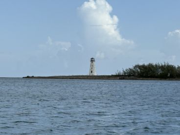 A picturesque view of a lighthouse standing tall against a backdrop of blue skies and calm waters, perfect for capturing the beauty of coastal landmarks.
