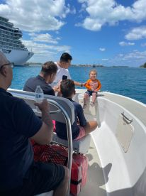A joyful family enjoys a boat ride with a child, capturing a moment of fun on the water against a backdrop of a cruise ship and clear blue skies.