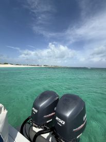 A clear view of outboard motors on a boat, with turquoise waters and a sandy beach in the background, perfect for exploring beautiful coastal destinations.