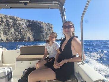 Two young women enjoy a sunny boat ride with stunning cliff views in the background, capturing the essence of a fun day on the water.