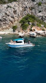 A lively group enjoys a summer day on a boat, with some swimming in the clear waters near a rocky beach — perfect for a fun day out on the water.