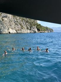 A lively group enjoys swimming in the clear blue waters near a stunning coastline, capturing the essence of summer fun on the water.