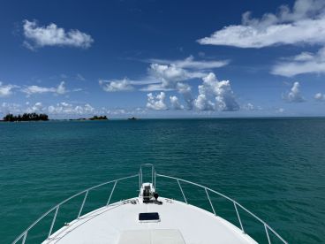 A stunning view from the bow of a boat cruising through crystal-clear turquoise waters, with picturesque islands and a vibrant sky in the background.
