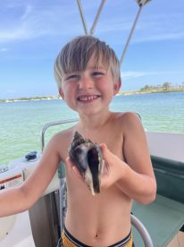 A young boy proudly holds a large shell while enjoying a day on the water, capturing a memorable moment of exploration and discovery.