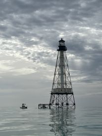 A lighthouse stands tall in the water with a small boat nearby, creating a serene maritime scene under a cloudy sky.