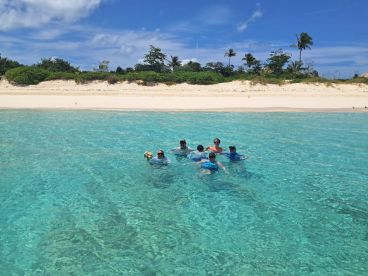 A joyful group enjoys a refreshing swim in the crystal-clear waters near a beautiful beach, perfect for family outings and fun in the sun.