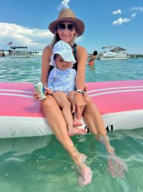 A joyful moment captured as a mother and her child relax on an inflatable mat in shallow water, enjoying a sunny day at the beach — perfect for family outings and summer fun.
