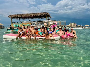 A joyful group of family and friends enjoys a fun day on the water, posing on a floating platform near a tiki boat, perfect for memorable celebrations and summer adventures.
