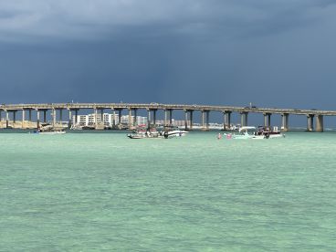 A vibrant scene featuring people enjoying the clear waters near a pier, with several boats anchored nearby — a perfect snapshot of a fun day on the water.