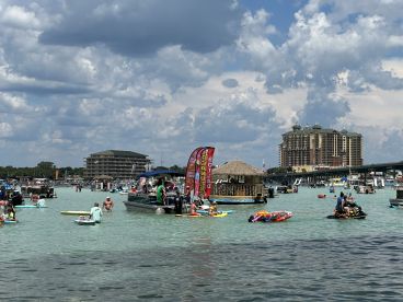 A vibrant scene at a sandbar with groups enjoying various water activities, including swimming and jet skiing, creating a lively party atmosphere.
