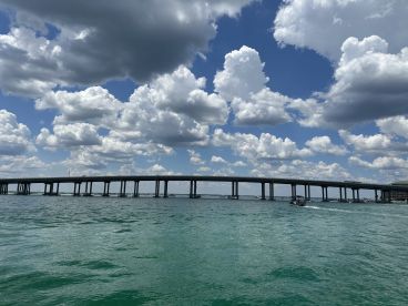 A scenic view of a bridge over turquoise waters, with a backdrop of fluffy clouds. The image captures the essence of a beautiful day on the water.