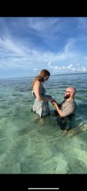 A romantic beach proposal unfolds in shallow waters, capturing a memorable moment between a couple against a stunning backdrop.