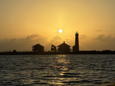A stunning sunset silhouette of a lighthouse and buildings along the shoreline, creating a picturesque scene perfect for evening boat cruises.