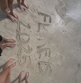 A group of friends celebrates their trip by writing 'FL Keys 2025' in the sand, capturing a memorable beach moment.
