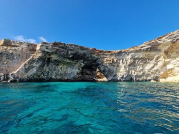 A stunning view of a rocky coastline with a cave entrance, surrounded by crystal-clear turquoise waters — a perfect destination for exploration and adventure.