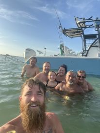 A joyful group enjoys a refreshing swim in shallow waters, with a pontoon boat in the background, perfect for a fun day out on the water.